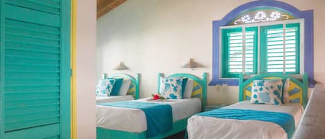 Una habitación con dos camas, cada una con cabecera azul y ropa de cama blanca, y una ventana con contraventanas azules.