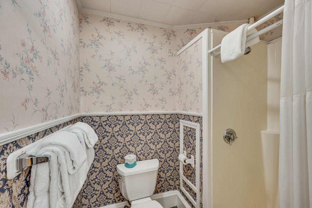 A bathroom with floral wallpaper, a toilet, a shower curtain, and a towel rack.