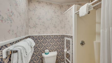 A bathroom with floral wallpaper, a toilet, a shower curtain, and a towel rack.