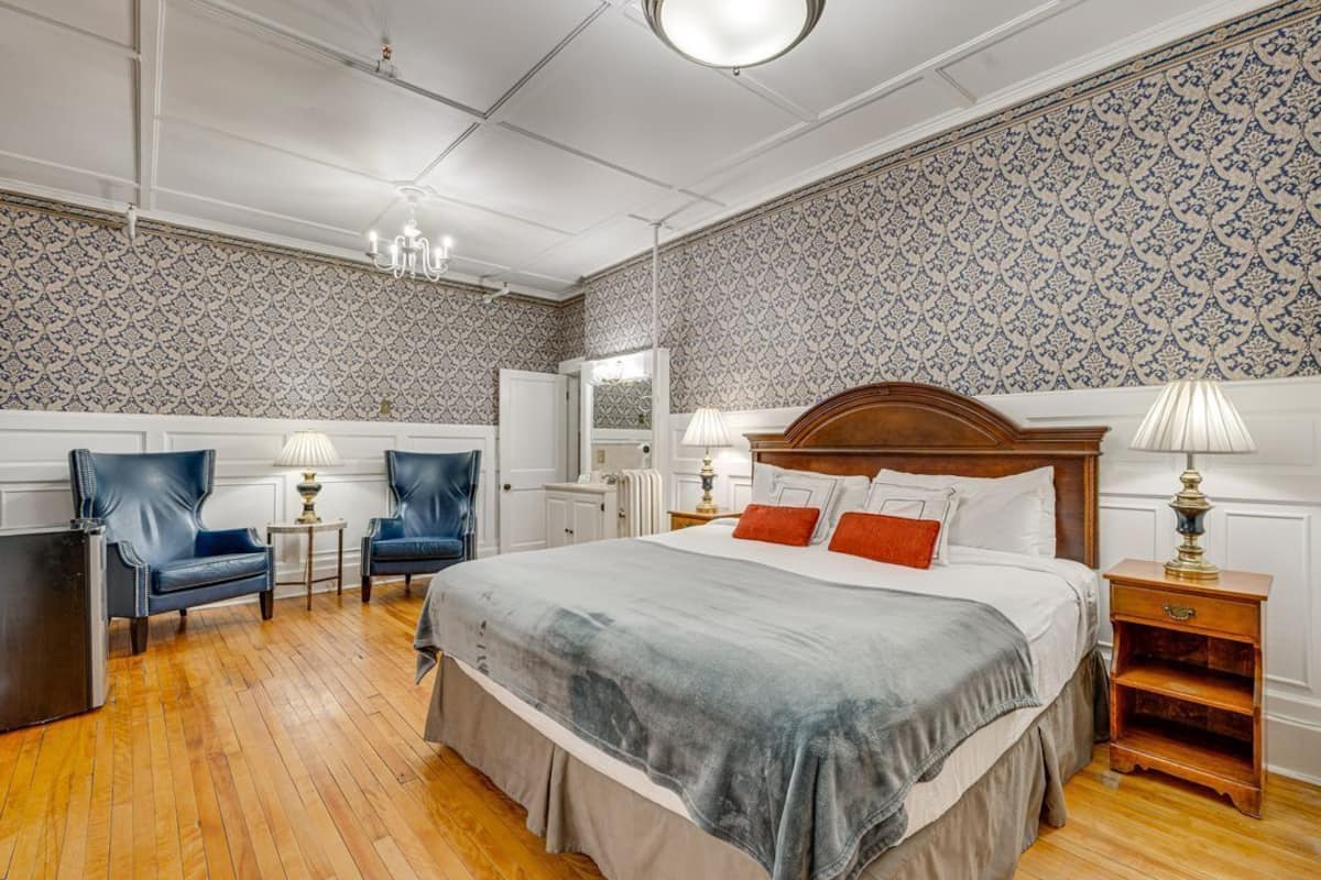 A bedroom with a large bed, two chairs, a nightstand, and a dresser.