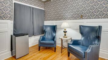 A room with two blue leather chairs, a small table with a lamp, a refrigerator, and patterned wallpaper.