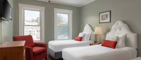 A hotel room with two beds, a red armchair, a wooden desk, and a ceiling fan.
