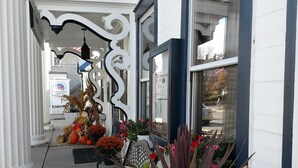 Un edificio con fachada blanca y detalles azules, que presenta un balcón con barandillas de metal ornamentadas y una jardinera con flores y calabazas.