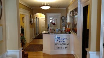 Un vestíbulo de hotel con un mostrador de recepción que indica 'Thayer Inn Reservations & Check In' y un arco que conduce al restaurante Grille One Eleven.