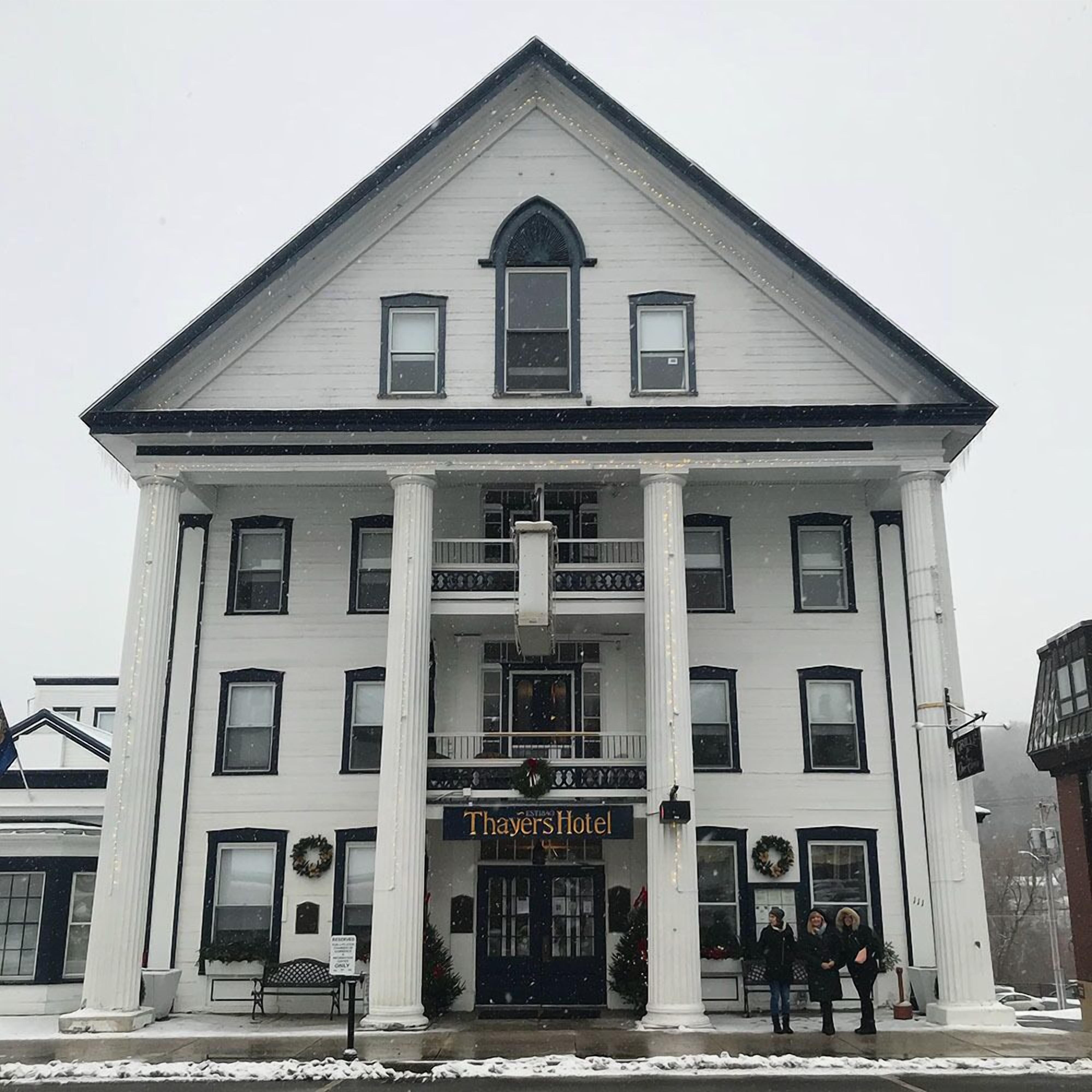 A white building with a central entrance, columns, and a sign reading "Thayers Hotel".