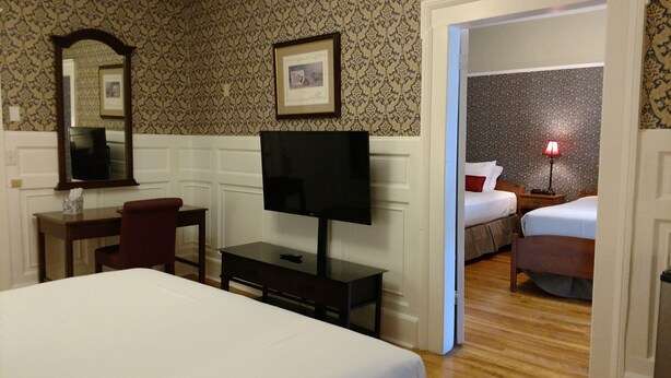 Habitación de hotel con cama, escritorio con televisor, silla, espejo y puerta que da a otra habitación.