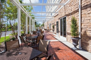 An outdoor patio with tables and chairs, a pergola, and a stone building with windows.