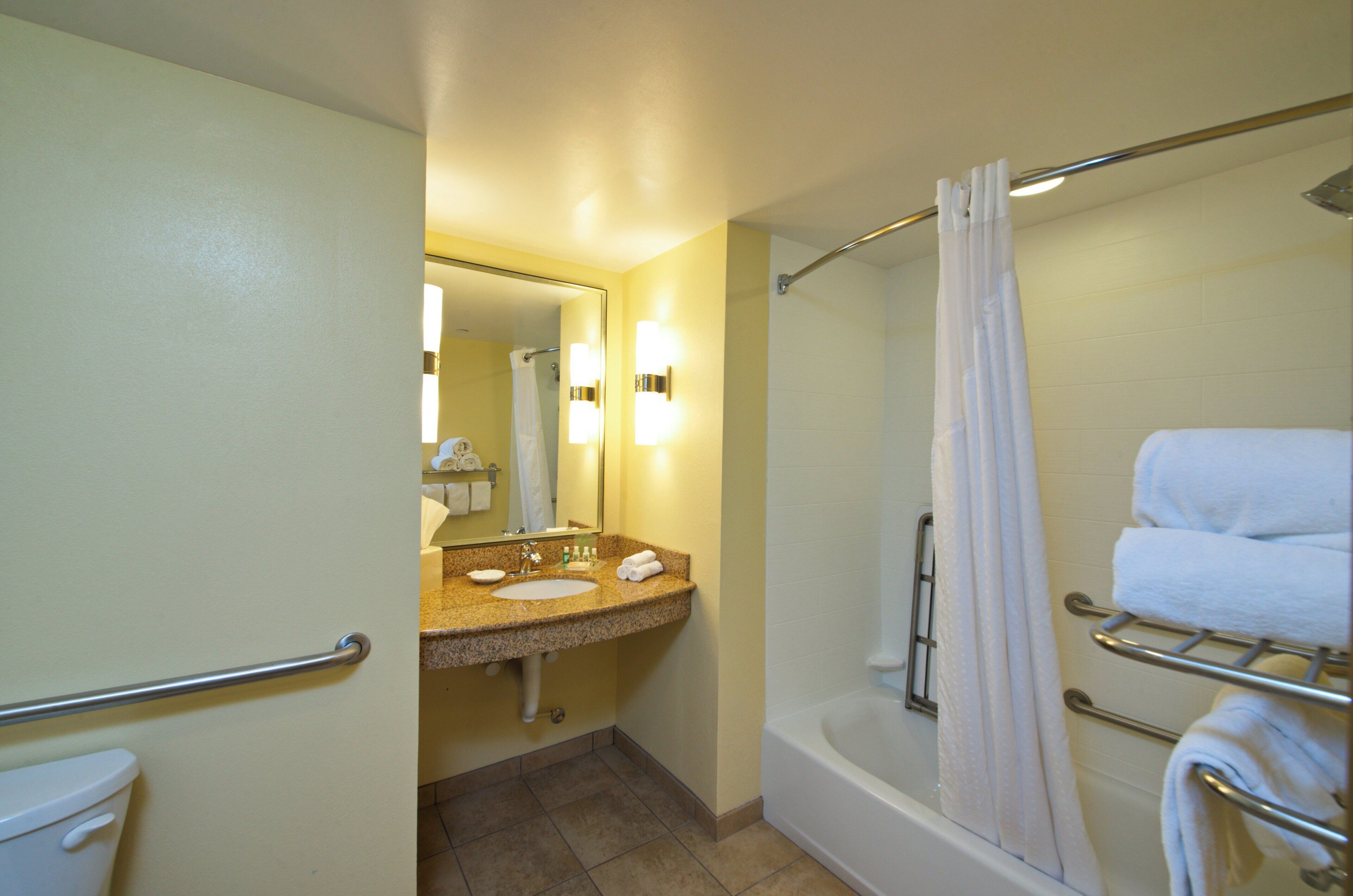 A hotel bathroom with a sink, mirror, towel rack, and shower.