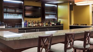 Zona de bar con encimera de granito, varias botellas de licor, vasos y un televisor de pantalla plana montado sobre la barra.