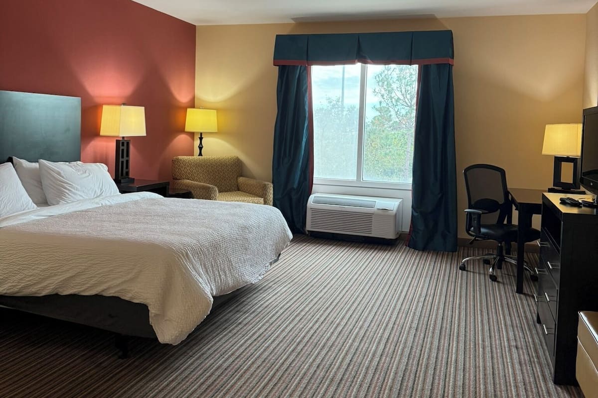 Habitació d'hotel amb un llit, dues làmpades de nit, un escriptori amb una cadira i una finestra gran amb cortines.
