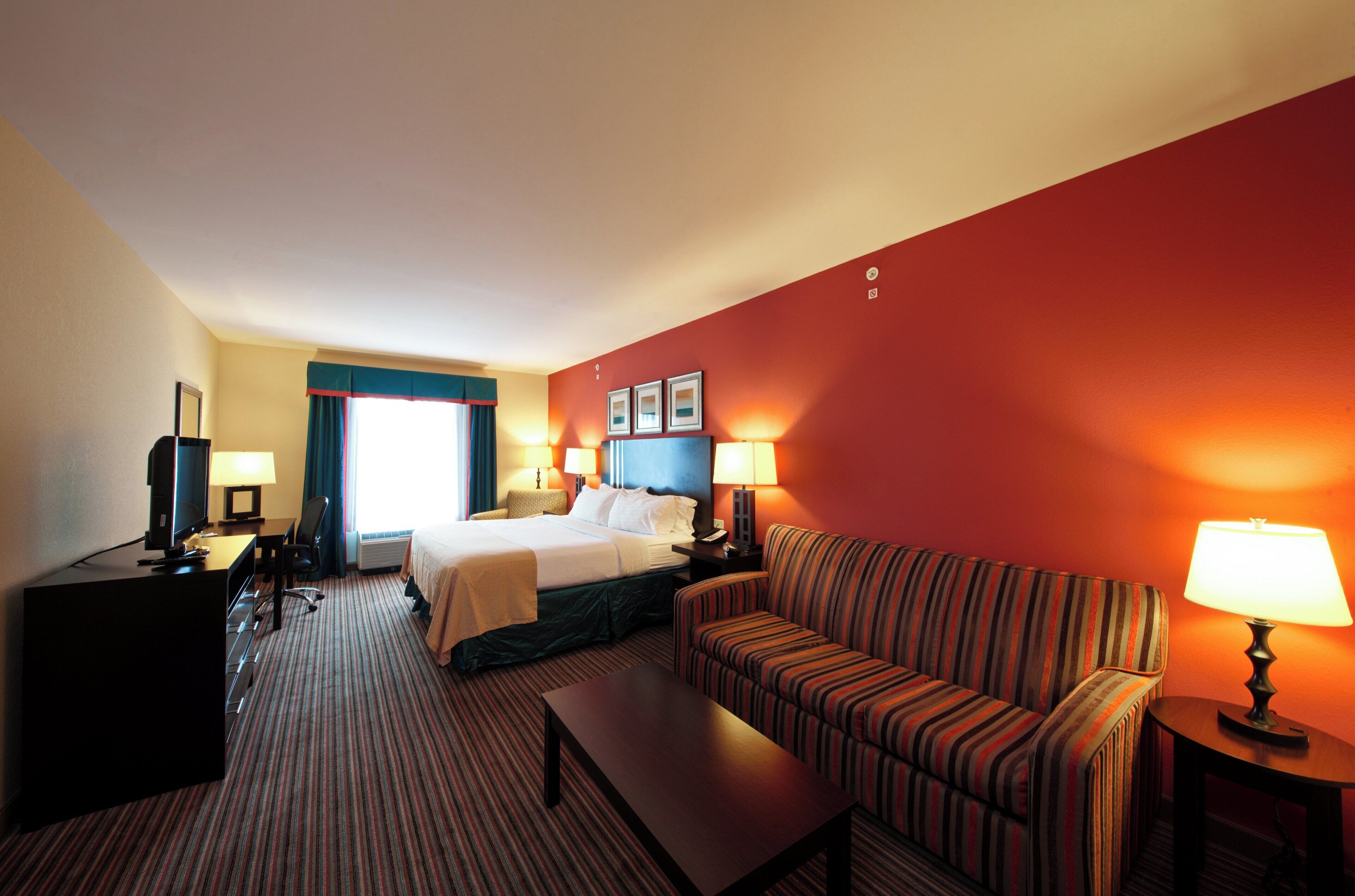A hotel room with a bed, a sofa, a desk with a computer, and a TV.