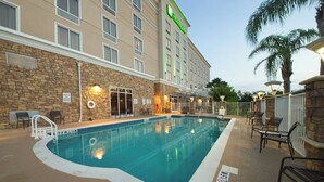 Zona de piscina de hotel con muro de piedra, sillas de descanso y señalización de socorrista de servicio.