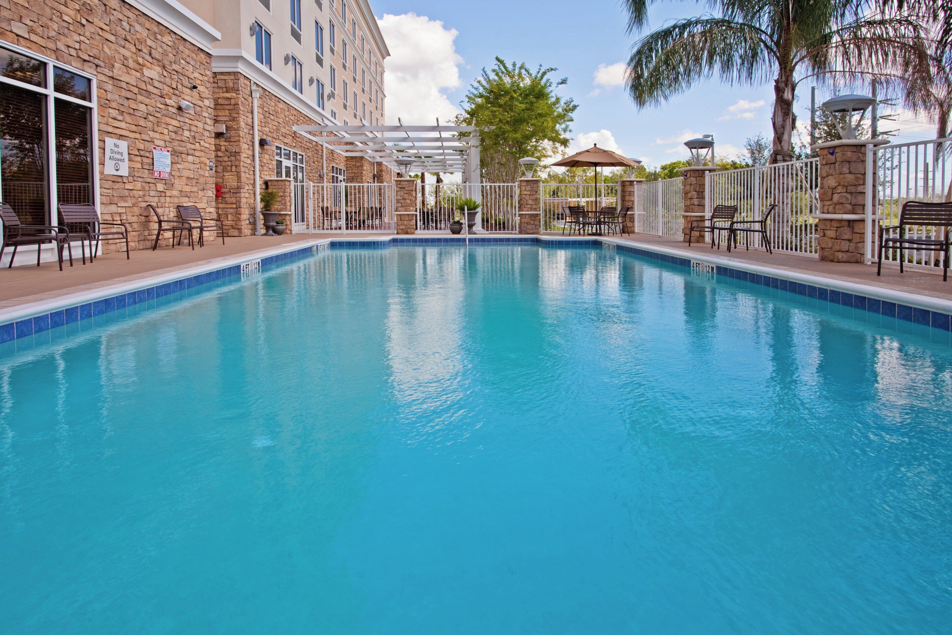 A swimming pool with a stone facade, outdoor seating, and a clear sky.