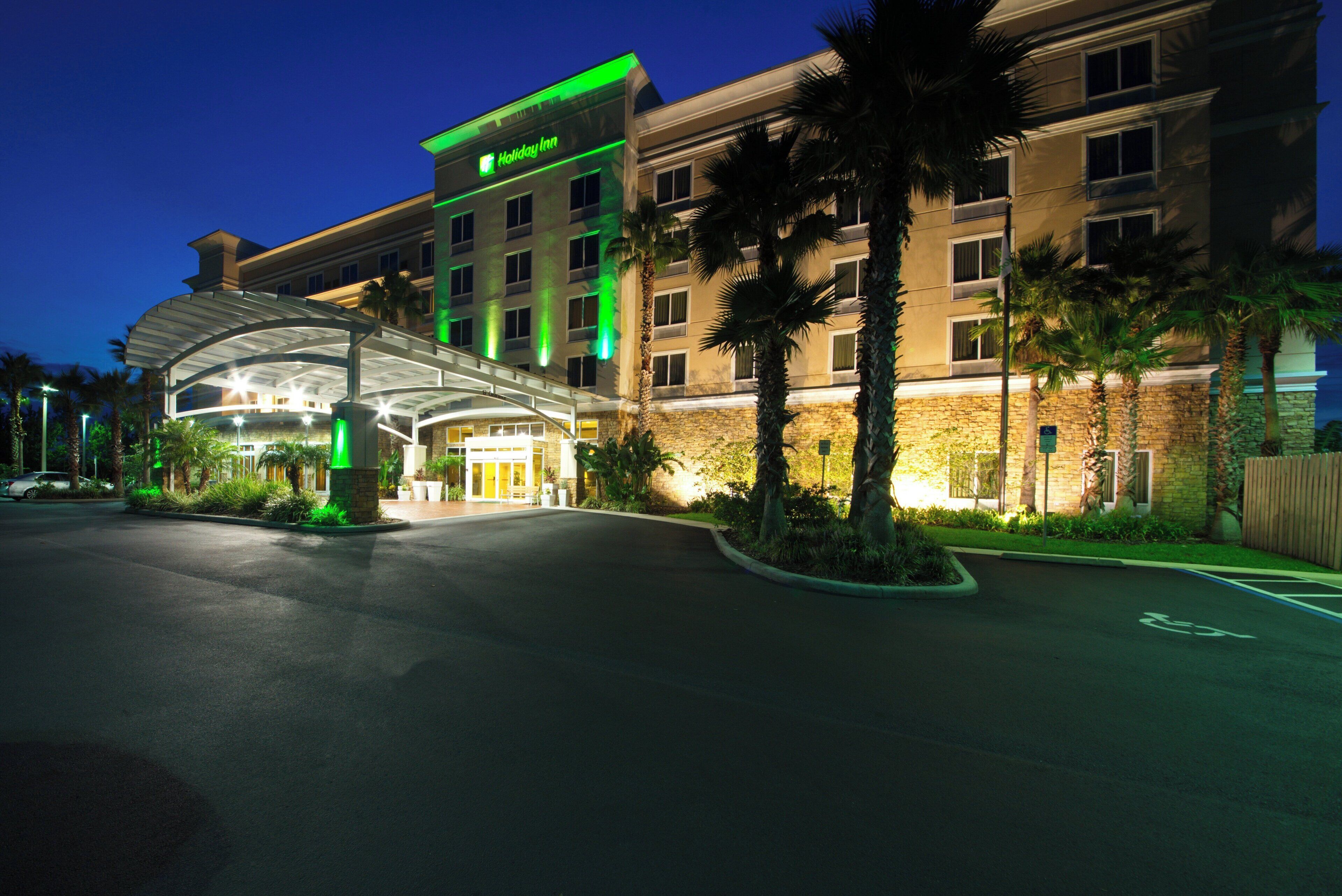 A Holiday Inn hotel with a covered entrance, palm trees, and a parking lot.