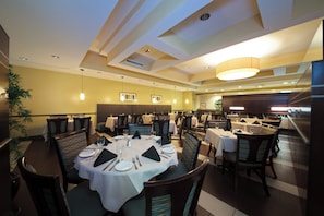 A dining area with tables set for four, chairs with striped upholstery, and pendant lighting.