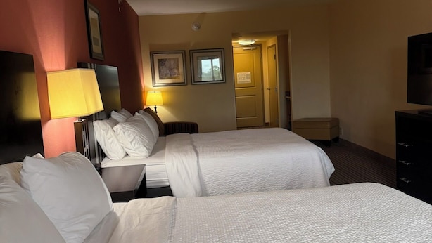 A hotel room with two beds, a desk, a lamp, and a television.
