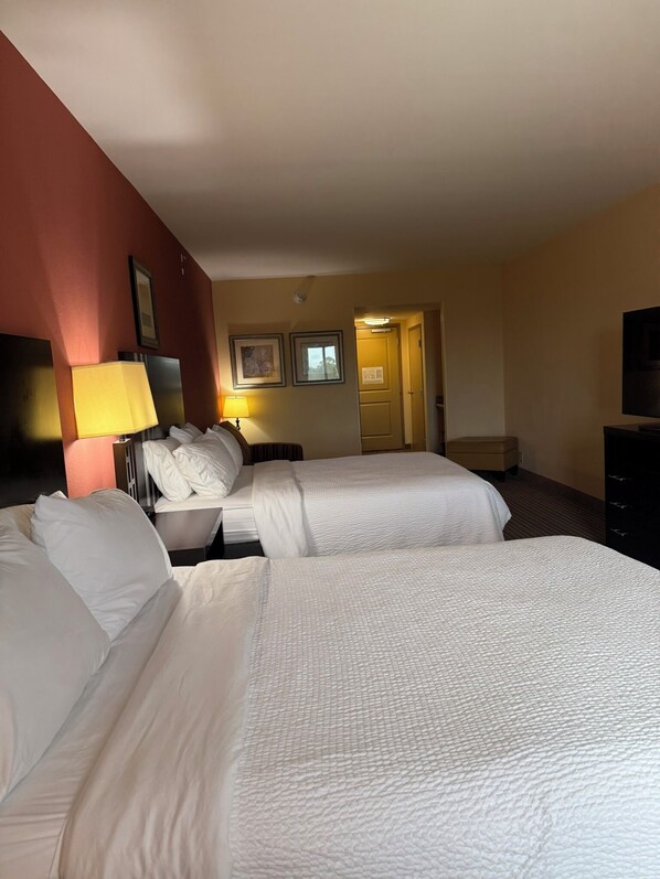 Habitación de hotel con dos camas, un escritorio, una lámpara y un televisor.