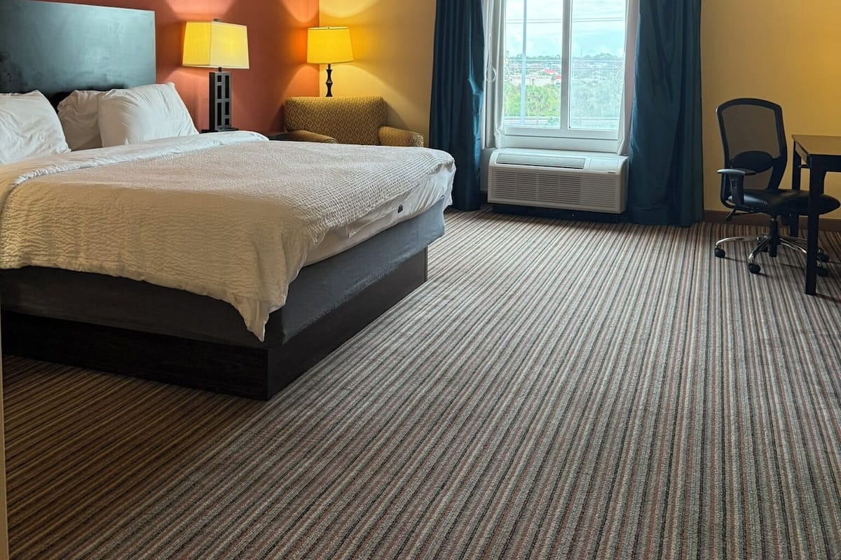 Habitació d'hotel amb un llit, dues làmpades de nit, una finestra amb cortines, una cadira i una taula.