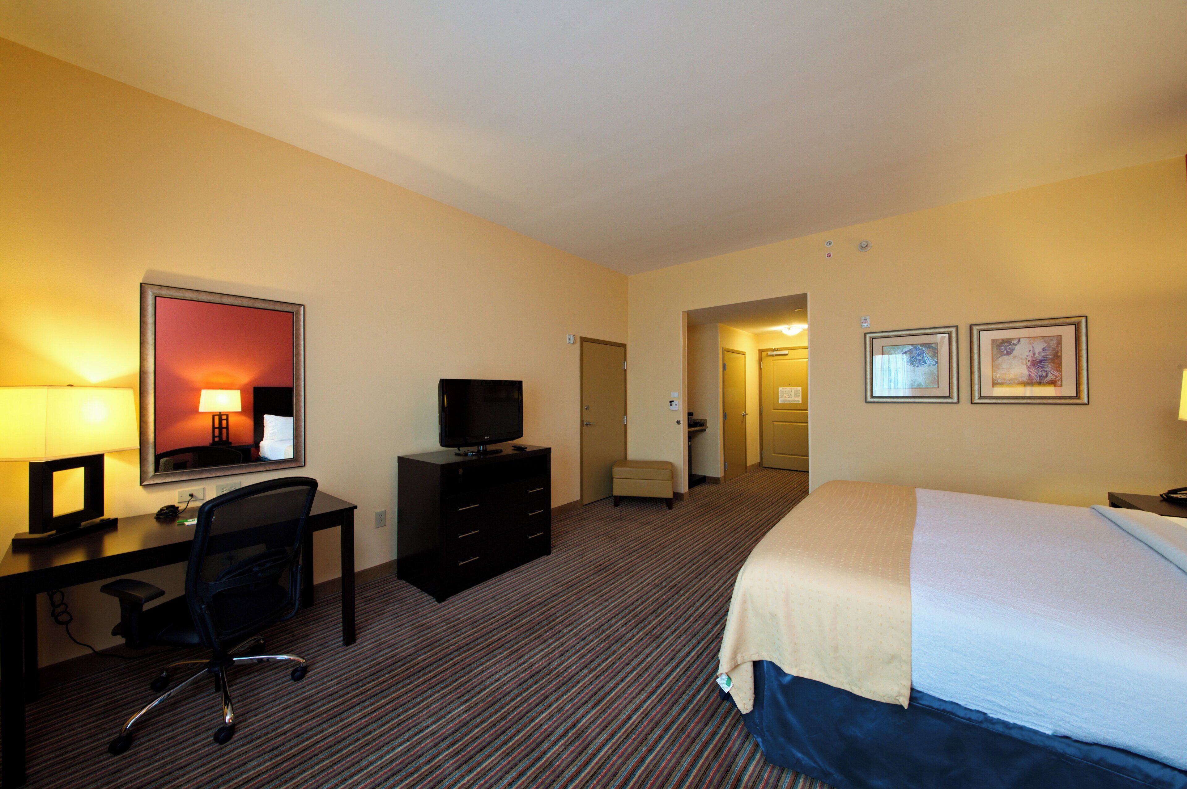 Habitación de hotel con cama, escritorio, silla, televisor y puerta que da a un baño.