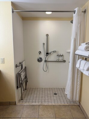 Un área de ducha pequeña con azulejos, una barra de apoyo, un perchero y un cabezal de ducha.
