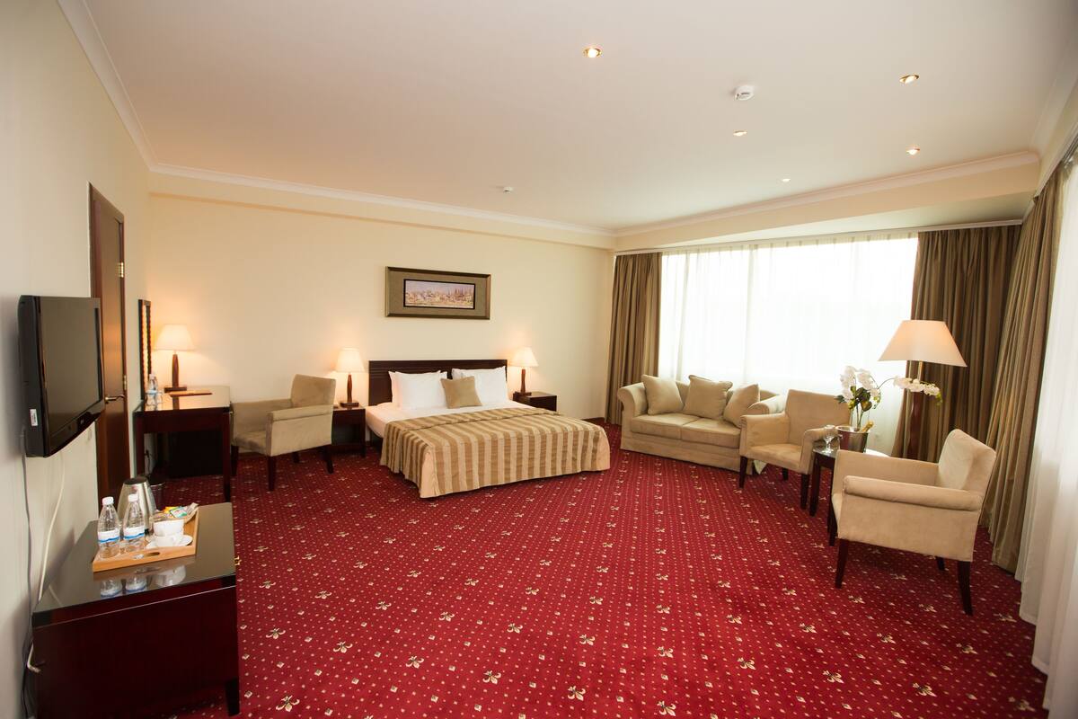 A hotel room with a large bed, two armchairs, a sofa, a TV, and a desk with a tray of items.