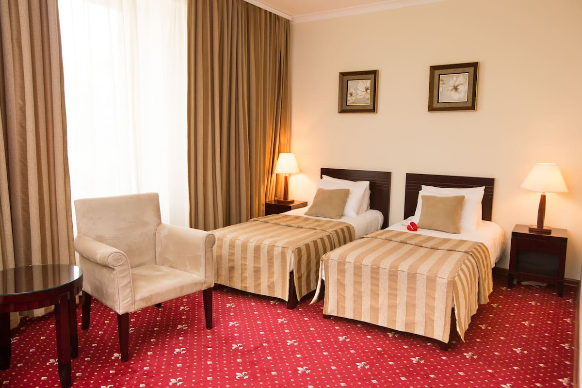 A hotel room with two beds, a chair, a table, and a lamp.