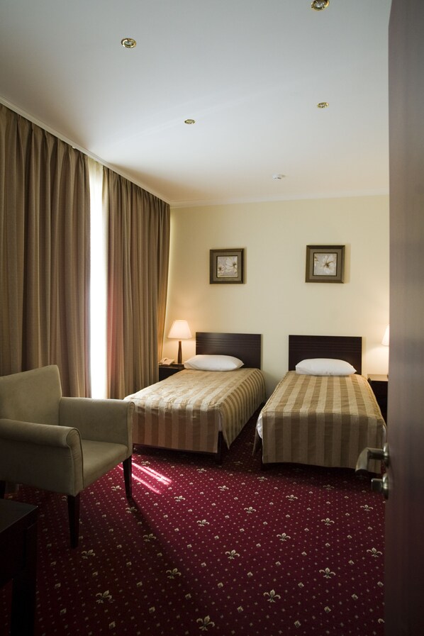 A hotel room with two beds, a chair, a desk, and a carpeted floor.