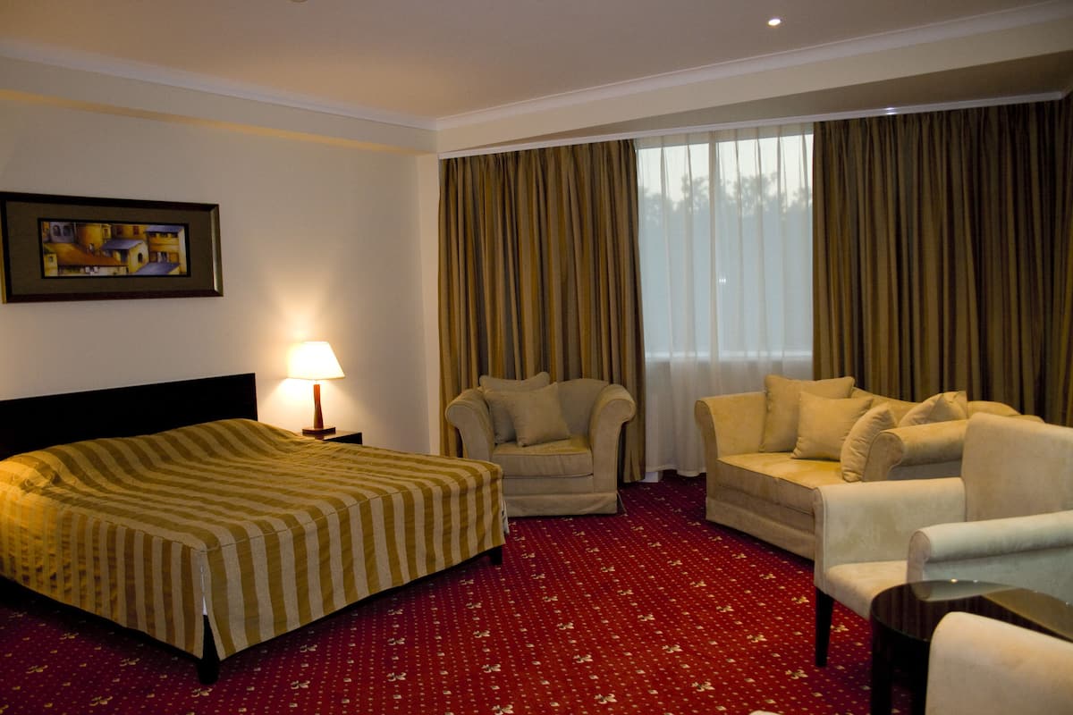 A hotel room with a bed, two armchairs, a sofa, a lamp, and a window with curtains.