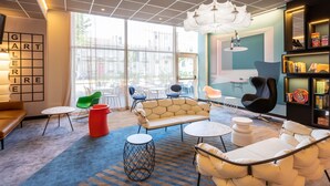 A modern lounge area with a sofa, chairs, a coffee table, and a bookshelf. - ibis Styles Bordeaux Meriadeck (Bordeaux)