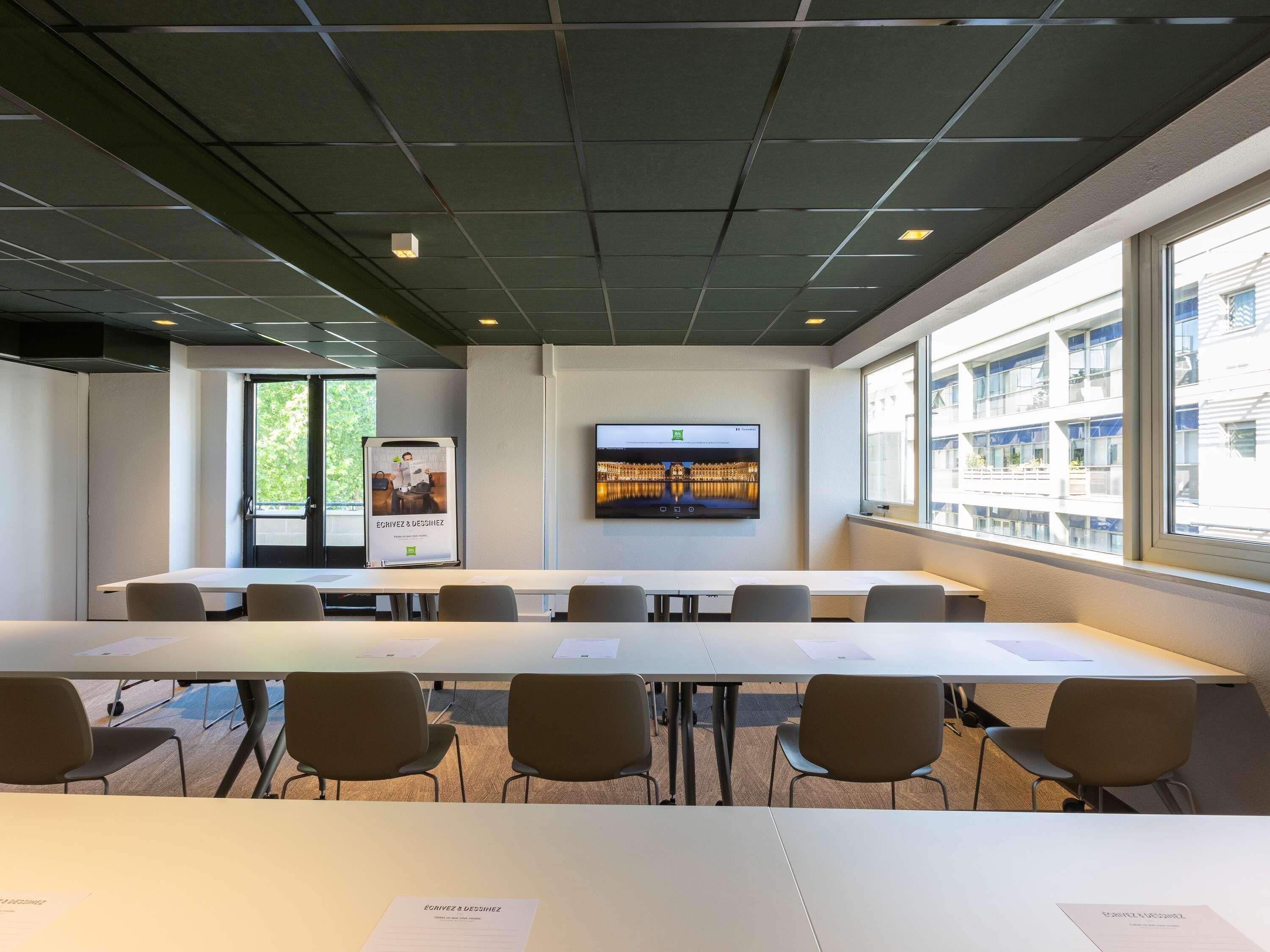 A conference room with a long table, chairs, a flat-screen TV, and a poster on the wall.