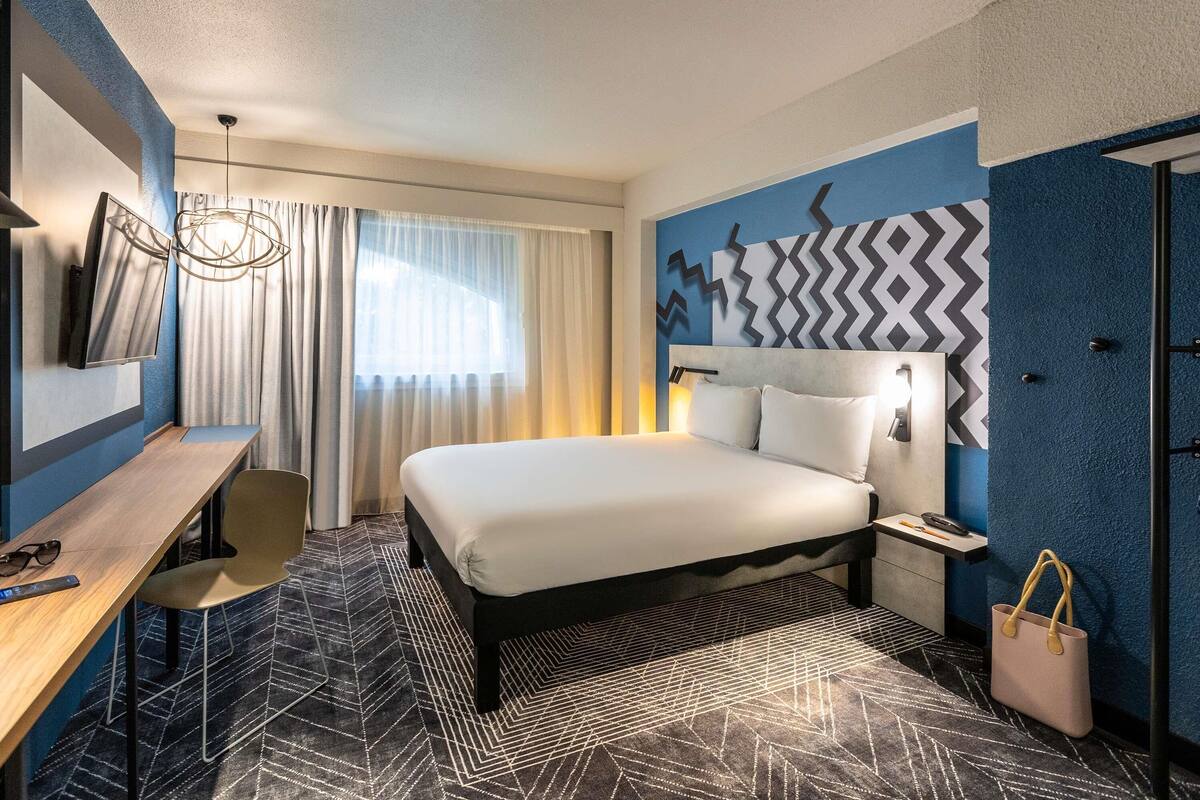 Una camera d'albergo con un letto, una scrivania, una sedia e una parete con motivo geometrico.