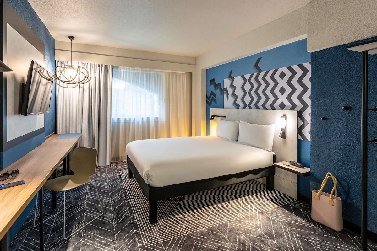 A hotel room with a bed, desk, chair, and a wall with a geometric pattern.