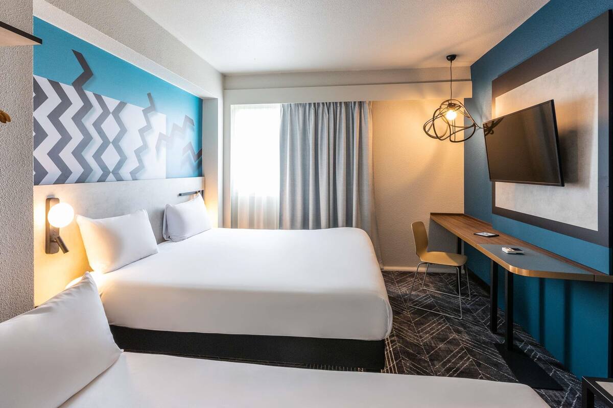 Una camera d'albergo con un letto grande, una scrivania, una TV e un moderno lampadario.