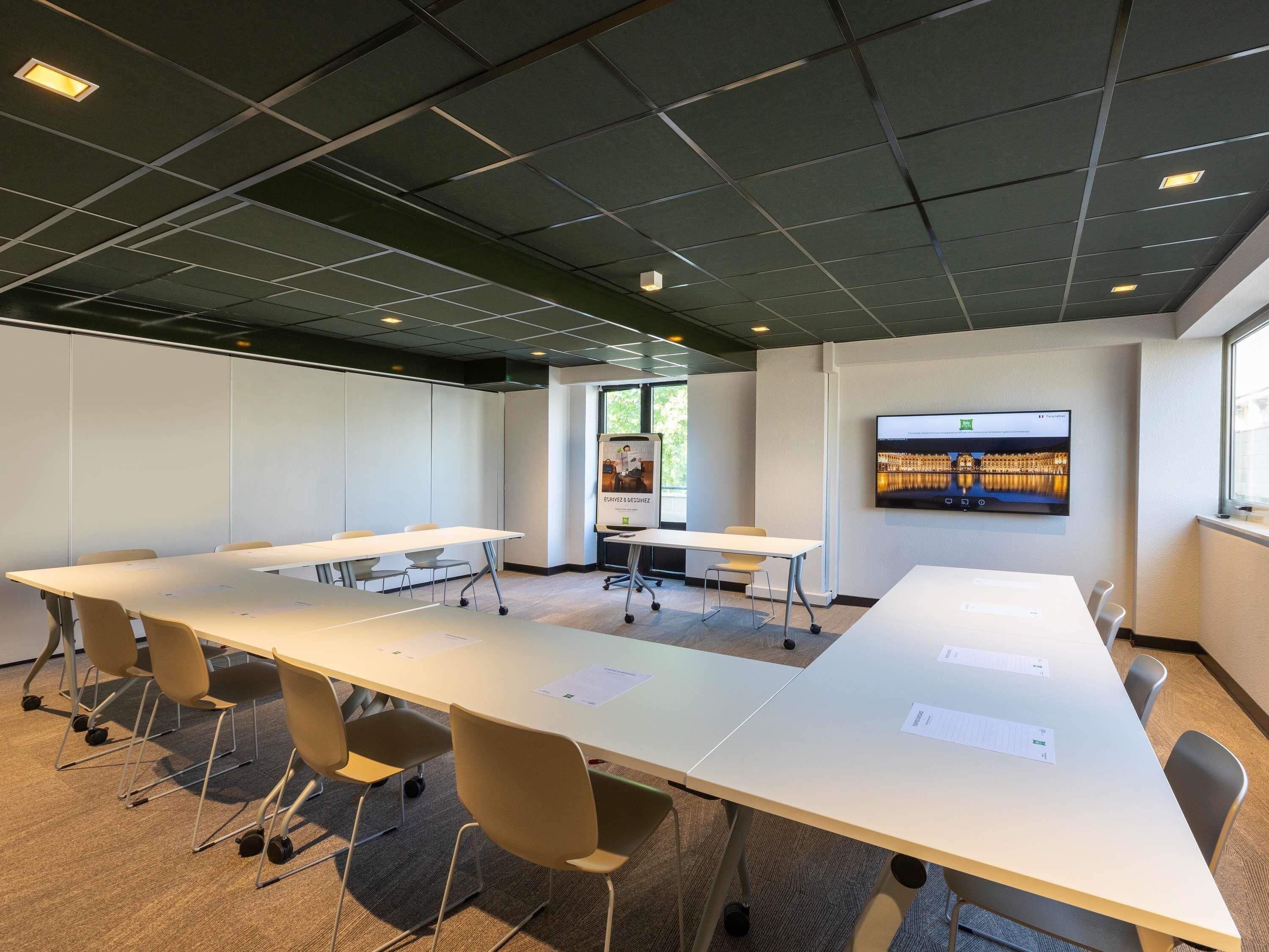 Un salón de conferencias con mesas blancas, sillas, una pantalla grande y un ventanal.