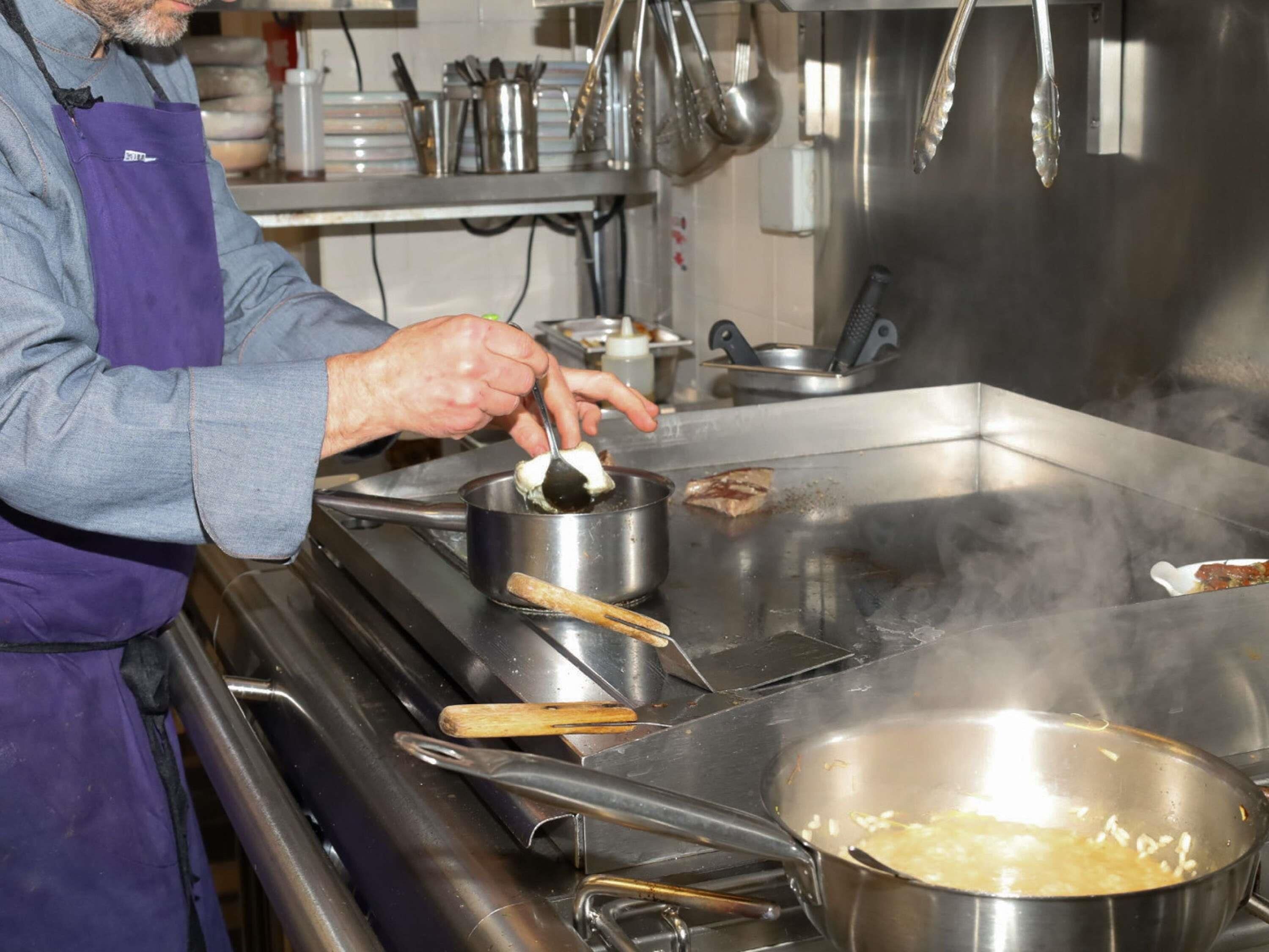 A chef preparing food in a professional kitchen with stainless steel equipment and a large cooking area.