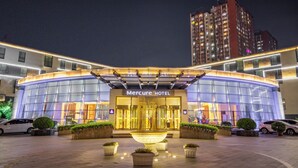Un hôtel moderne doté d’une façade en verre, d’une fontaine centrale et d’une entrée bien éclairée.