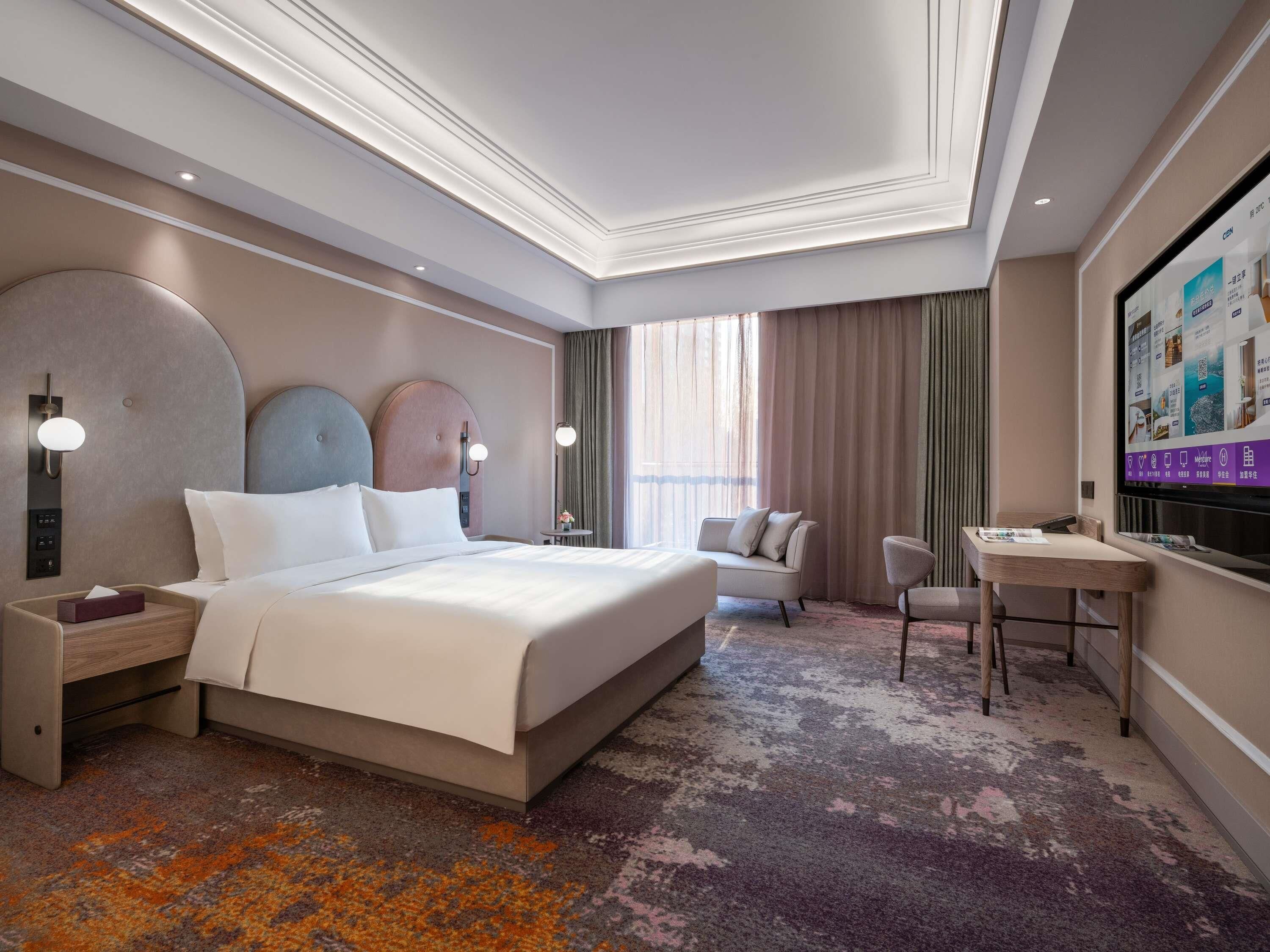 A hotel room with a large bed, bedside tables, a desk, a chair, and a television.