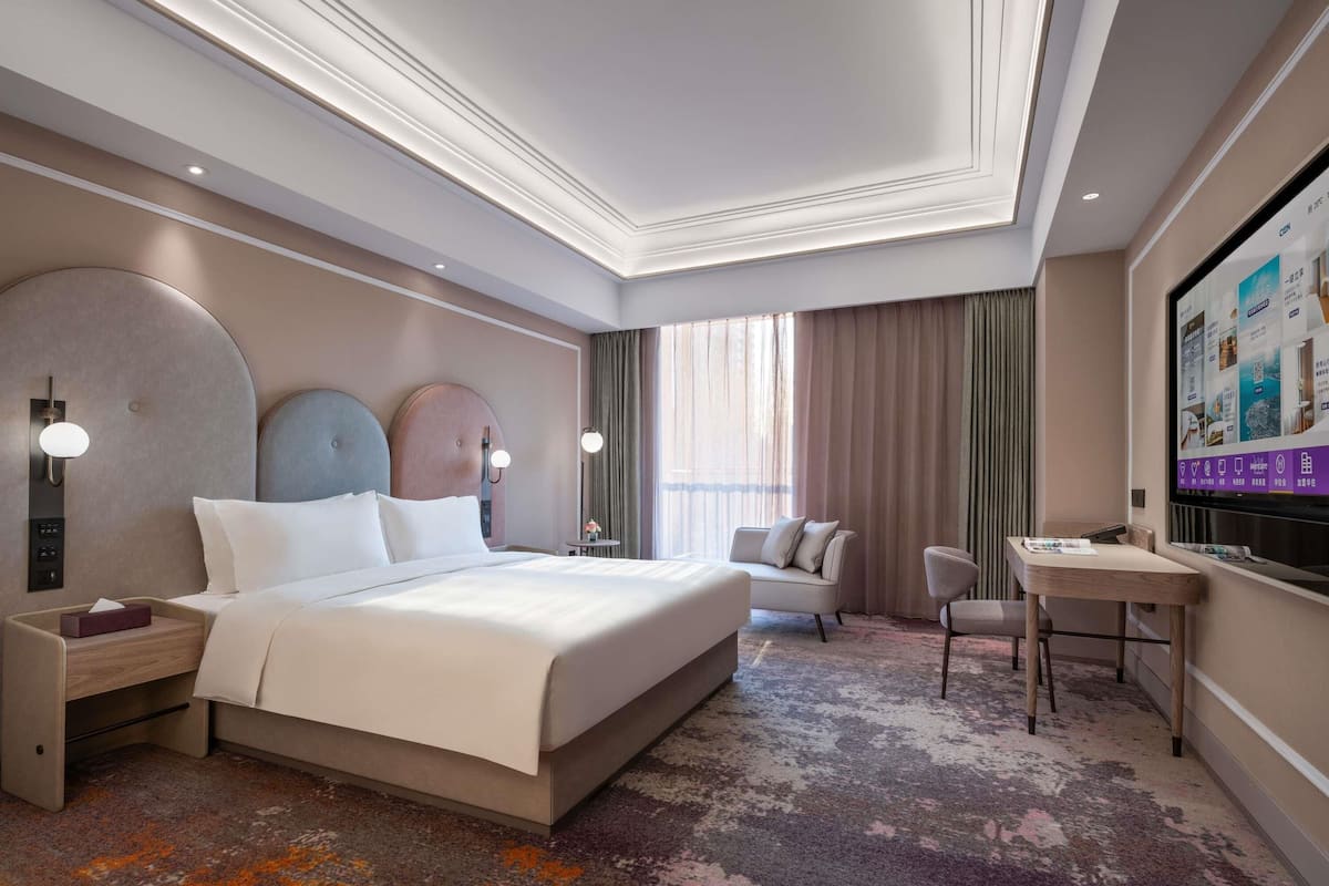 A hotel room with a large bed, bedside tables, a desk, a chair, and a television.