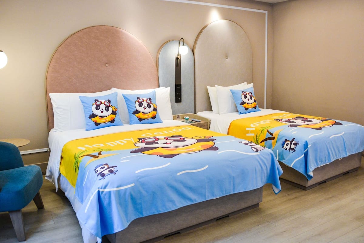 A hotel room with two beds, each with a panda-themed bedspread, a round headboard, and a small round table.