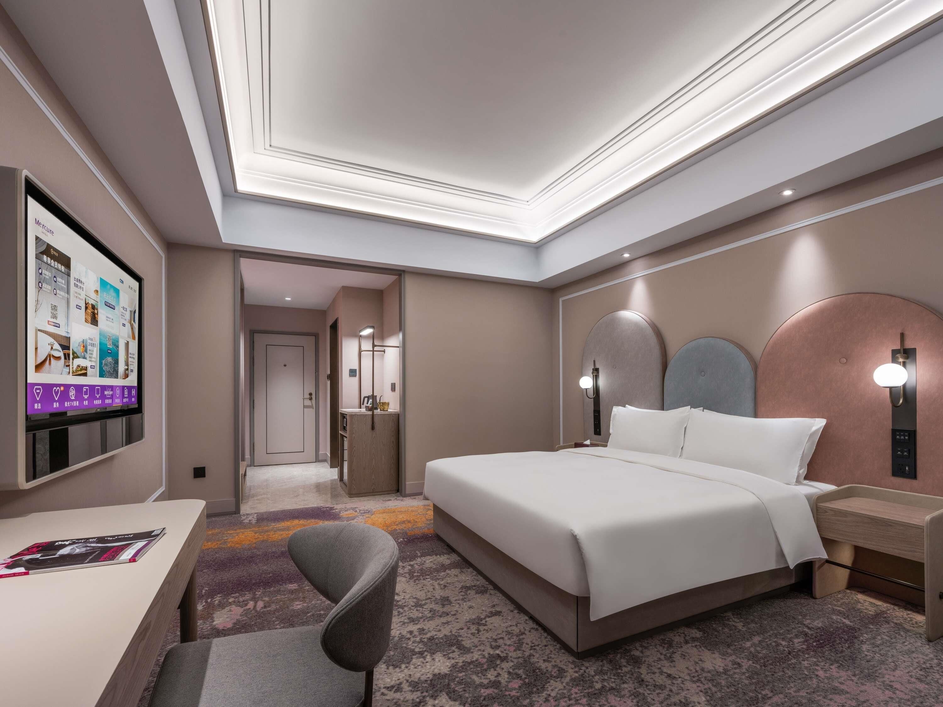 Una moderna camera d'hotel con un letto grande, una scrivania, una sedia e una televisione che mostra i servizi offerti.