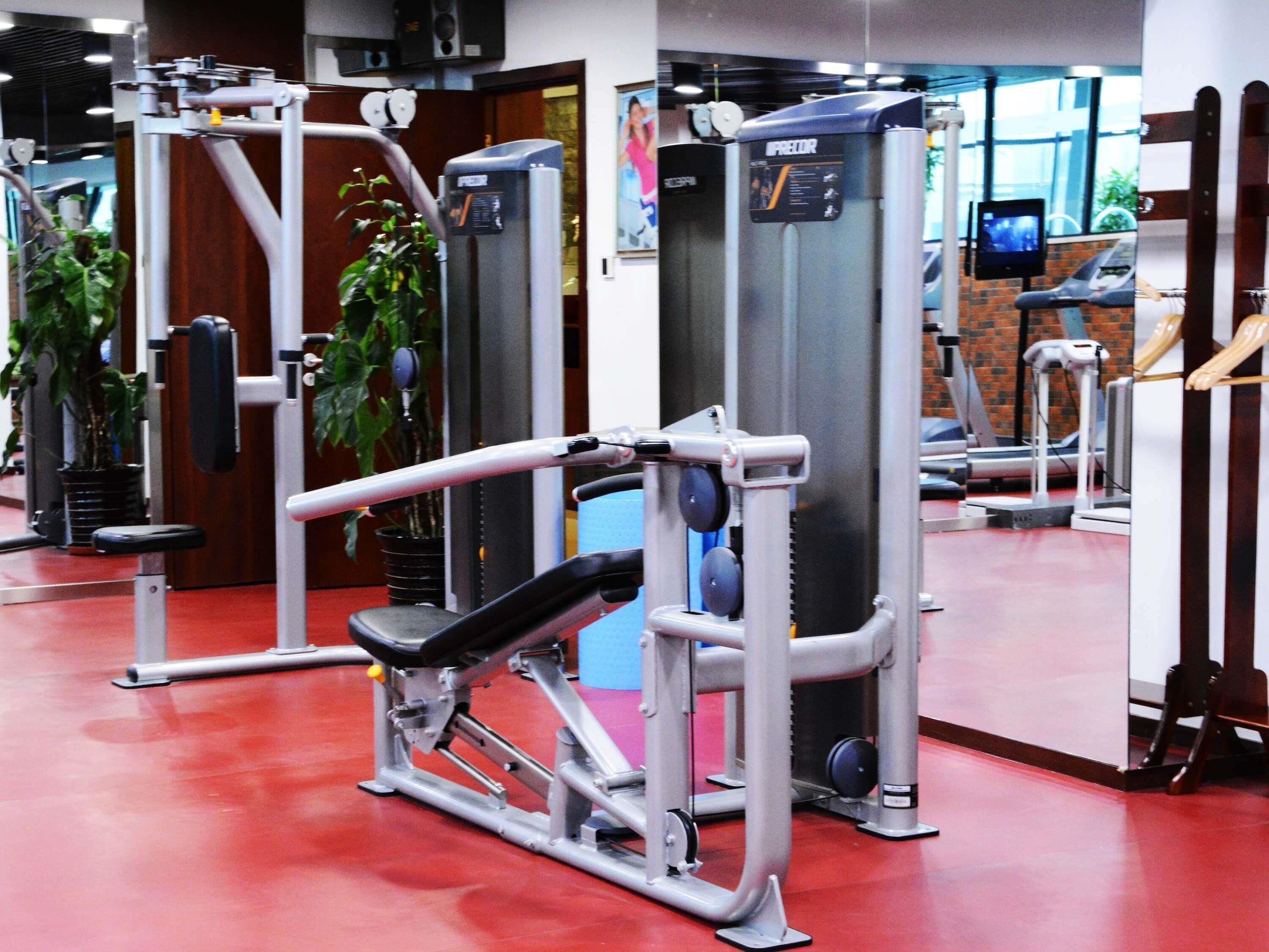 Une salle de sport équipée de matériel d’exercice, d’un tapis de course et d’un miroir qui reflète l’espace.