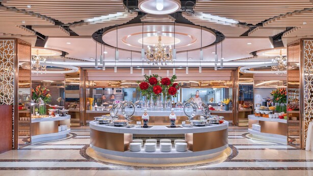 Un hall d’hôtel moderne avec un buffet central, des lustres et un plafond décoratif.
