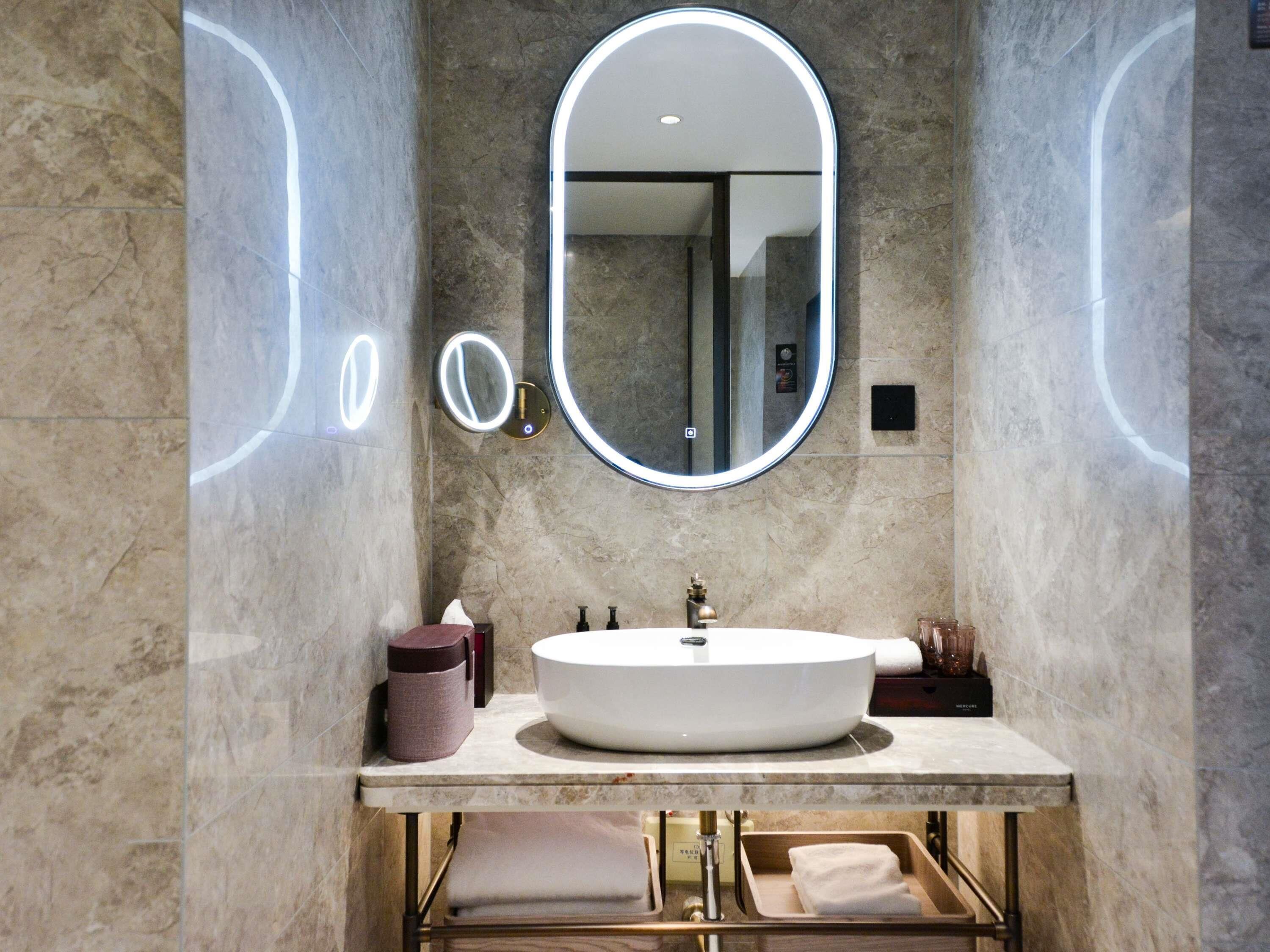 Un baño moderno con un espejo ovalado grande, un lavabo redondo y un perchero para toallas.