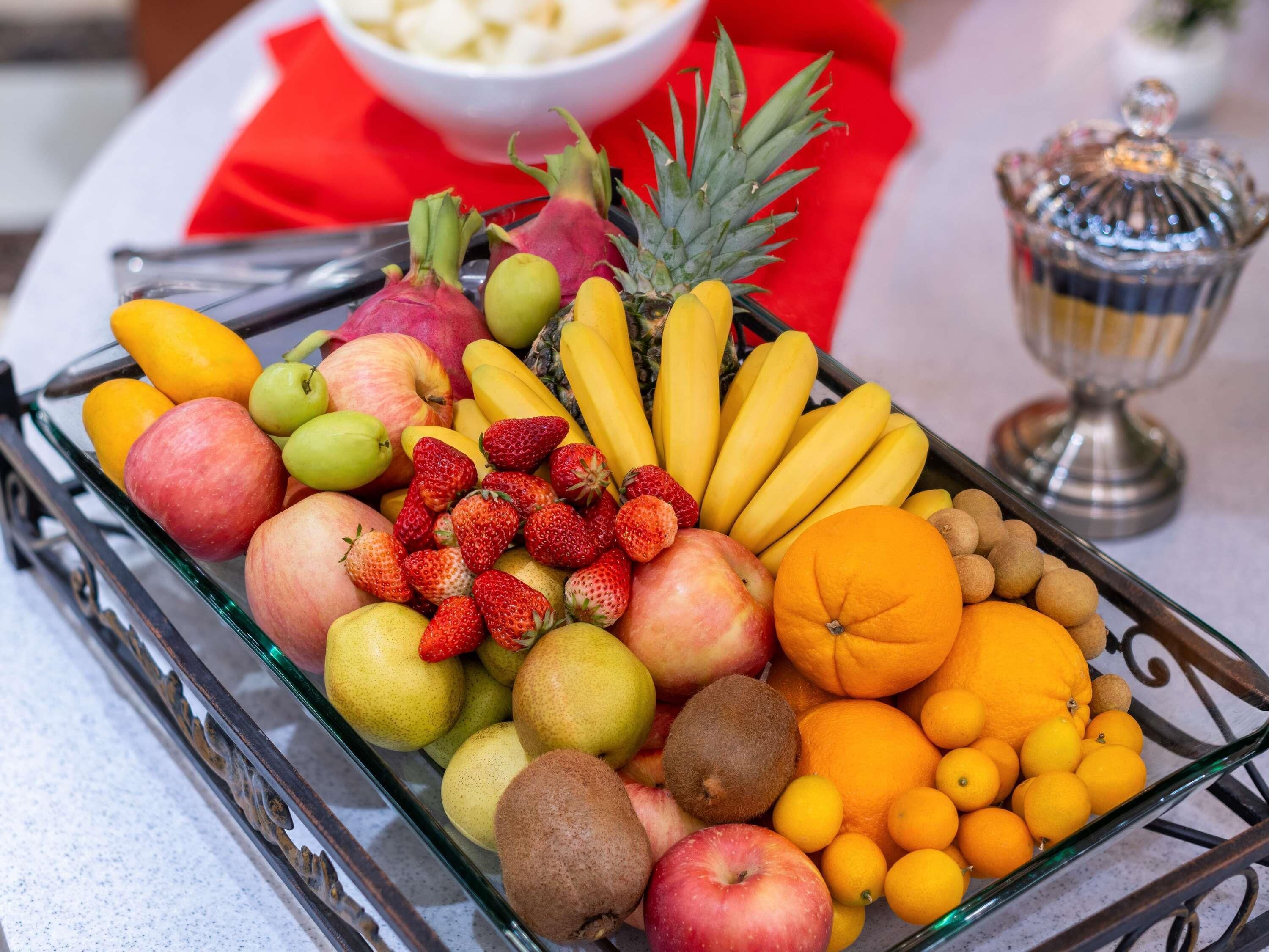 A glass tray filled with a variety of fruits including apples, bananas, oranges, and kiwis.