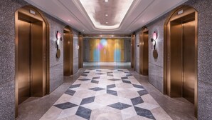 Un couloir moderne avec un sol à motifs géométriques, deux ascenseurs et un luminaire central.