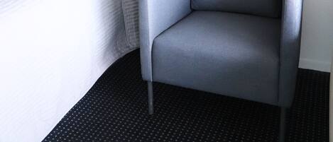 Habitación de hotel con cama, un sillón gris, pared de acento roja y lámpara en el techo.