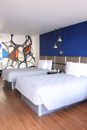 Ein Hotelzimmer mit zwei Betten, einem modernen abstrakten Wandbild, einer blauen Akzentwand und einem Holzboden.