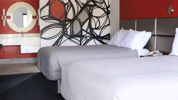 A modern hotel room with a large bed, a round mirror, a red accent wall, abstract art, and a black and white patterned floor.