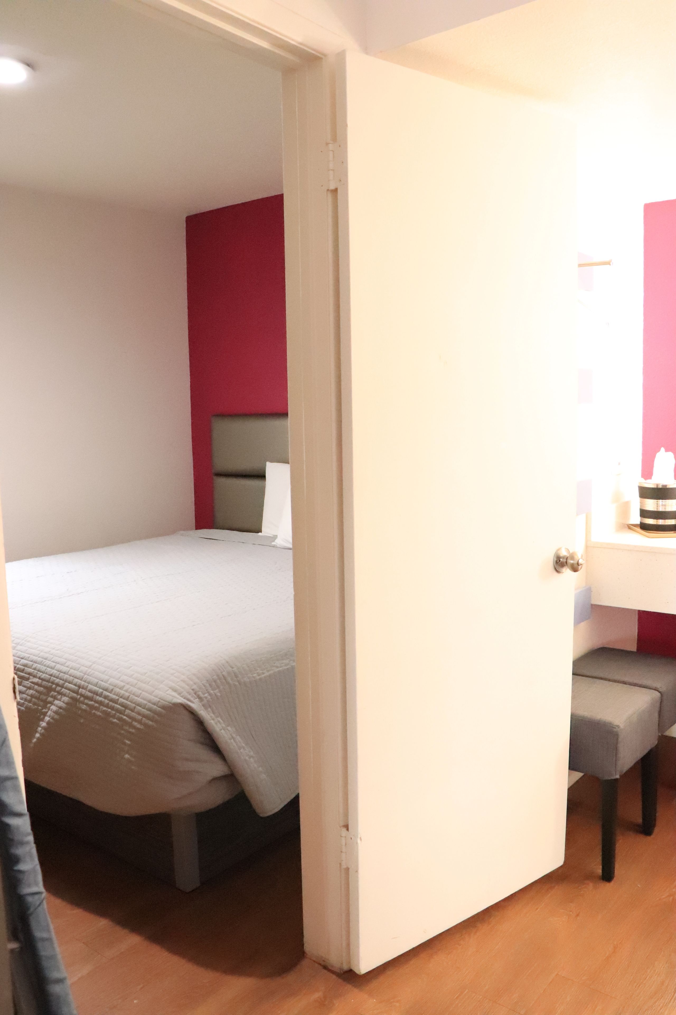 A bedroom with a bed, a bedside table, and a door leading to another room.