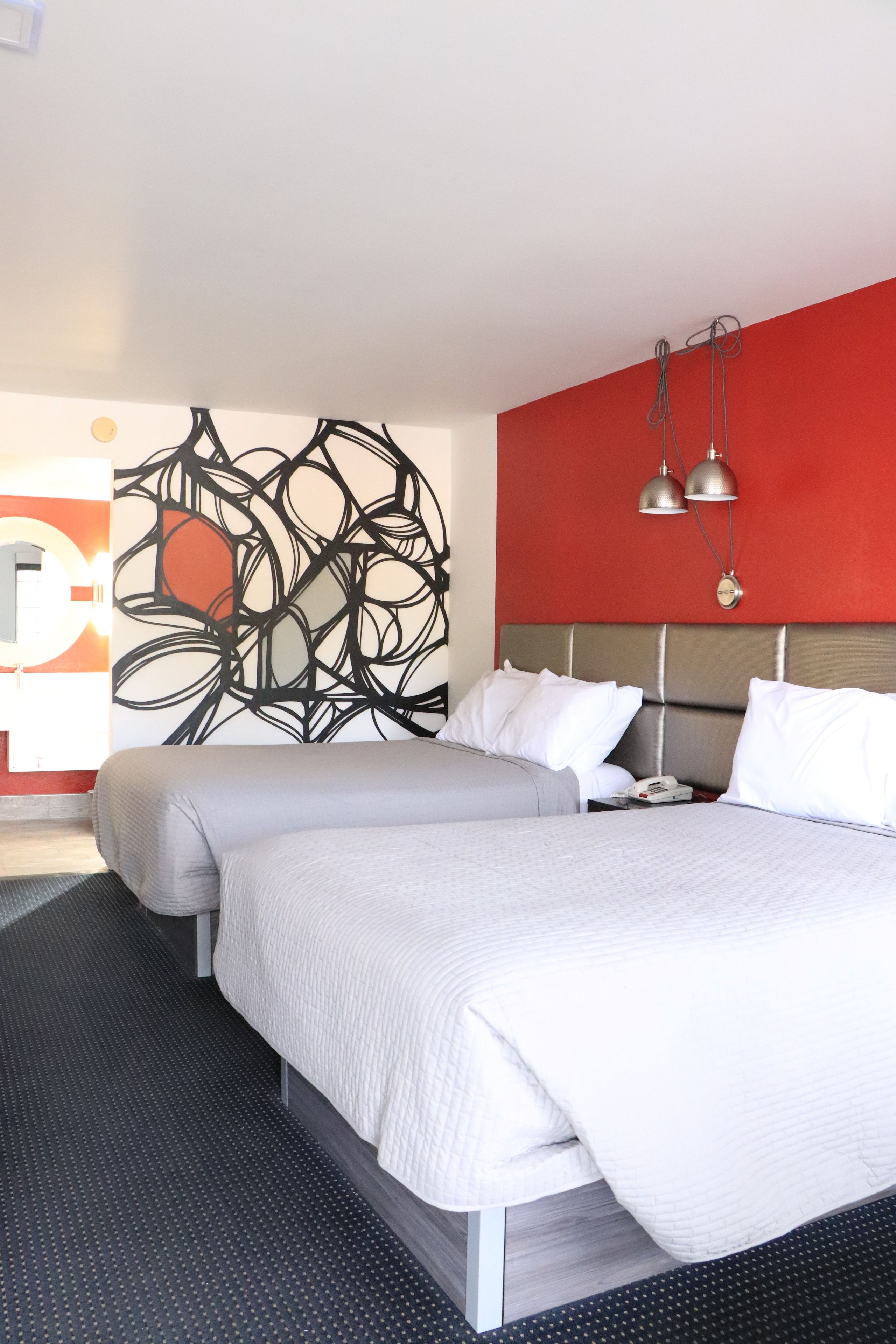 Habitación de hotel con una cama grande, dos mesitas de noche, una pared de acento roja y arte abstracto en la pared.
